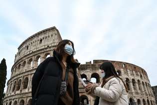 Turistas usam máscaras de proteção ao visitar o monumento do Coliseu, em Roma